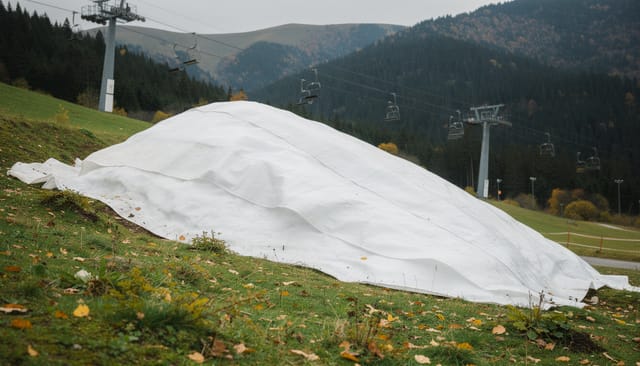Illustration: Huge pile of snow covered with white insulated blankets on a green mountain slope in autumn
